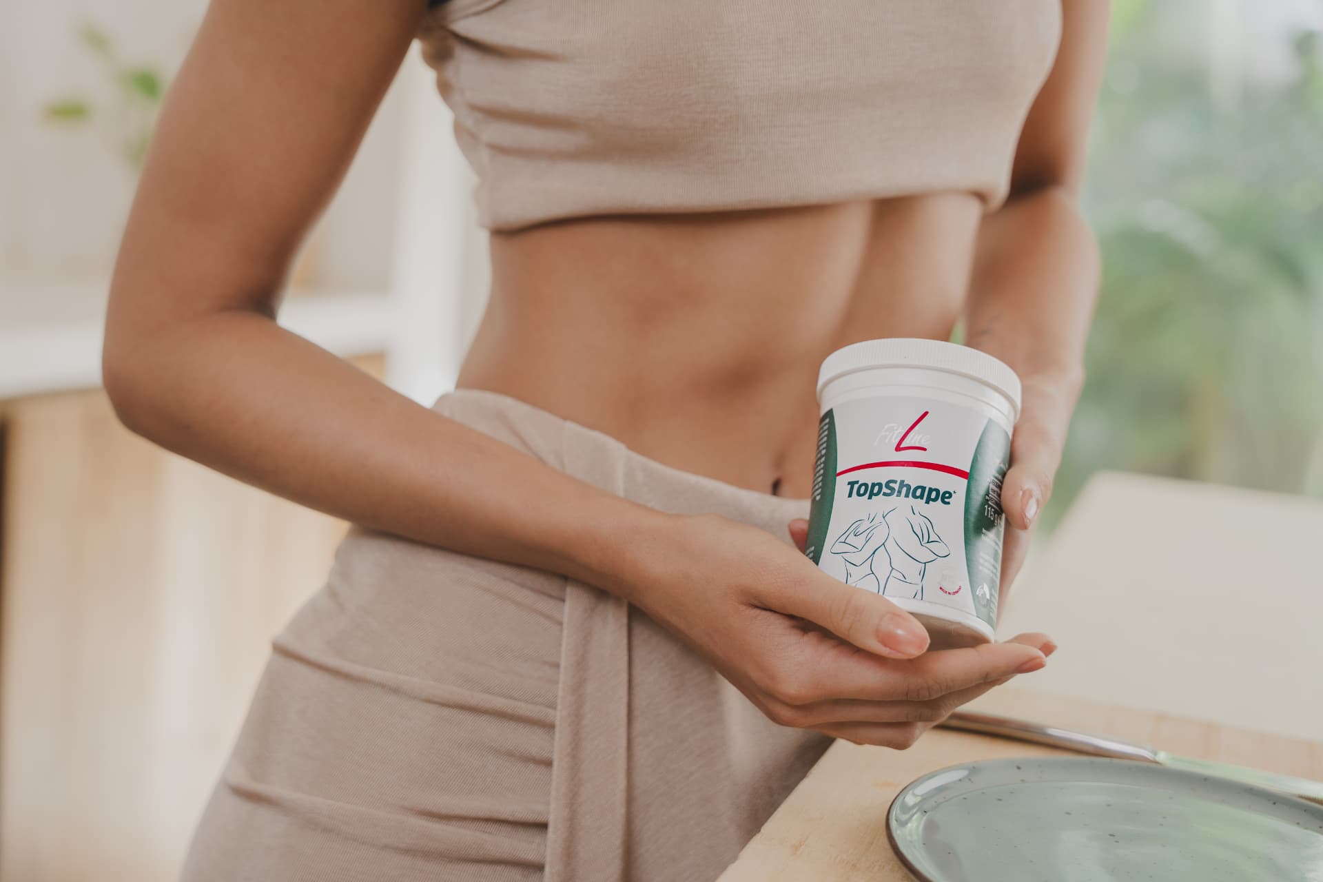 Vrouw houdt een pot FitLine TopShape vast aan de eettafel