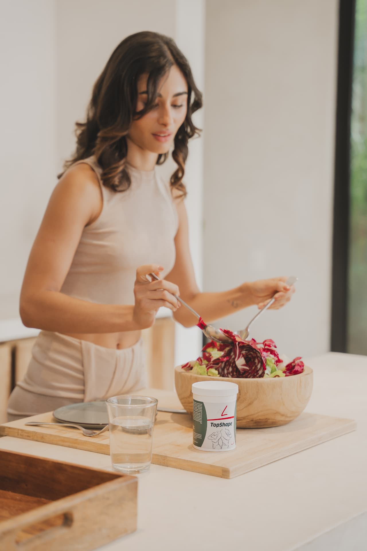 Vrouw schept een portie salade op met een pot FitLine TopShape op tafel