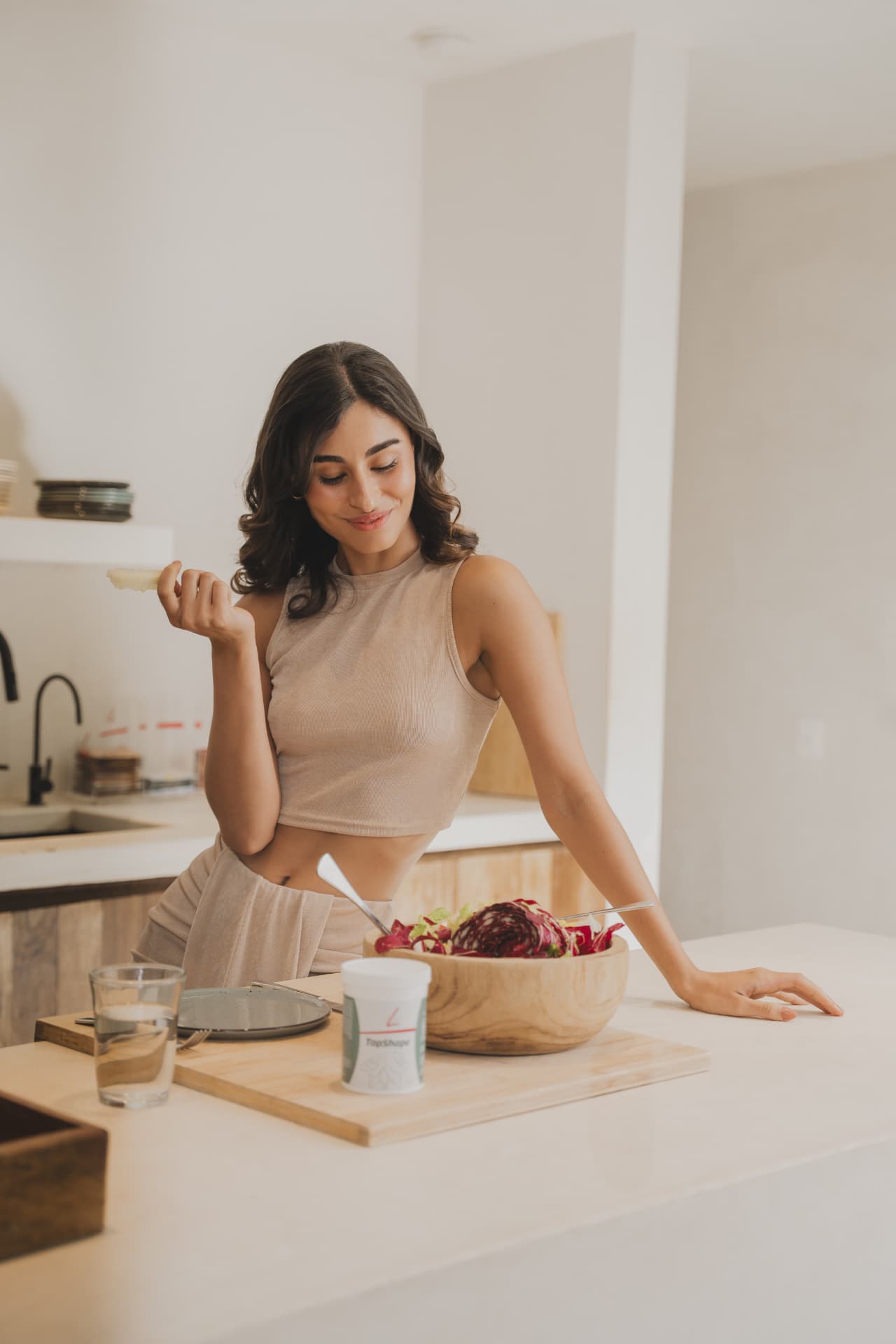 Vrouw eet thuis een salade met FitLine TopShape en een glas water erbij
