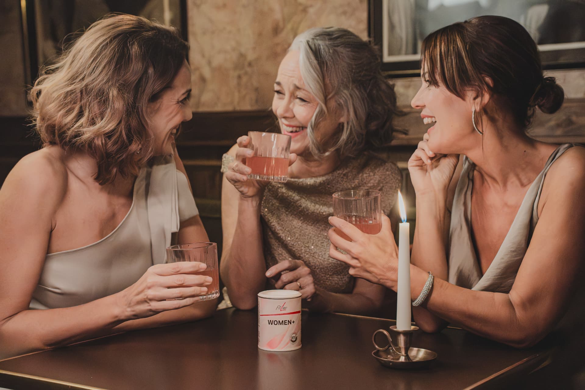 Drie lachende vrouwen aan tafel met glazen en een pot FitLine WOMEN+
