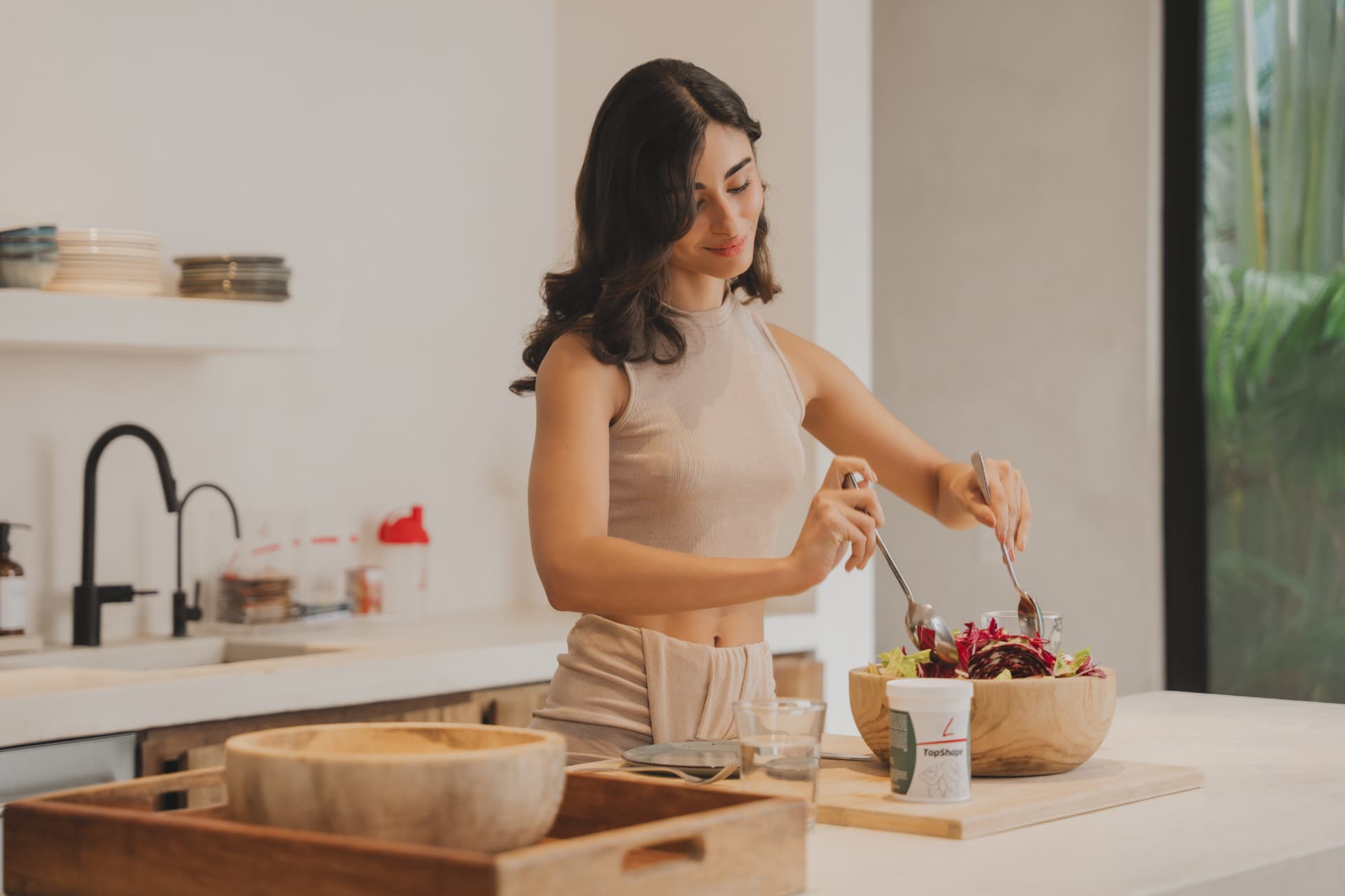Vrouw maakt een salade klaar in de keuken met FitLine TopShape op het werkblad