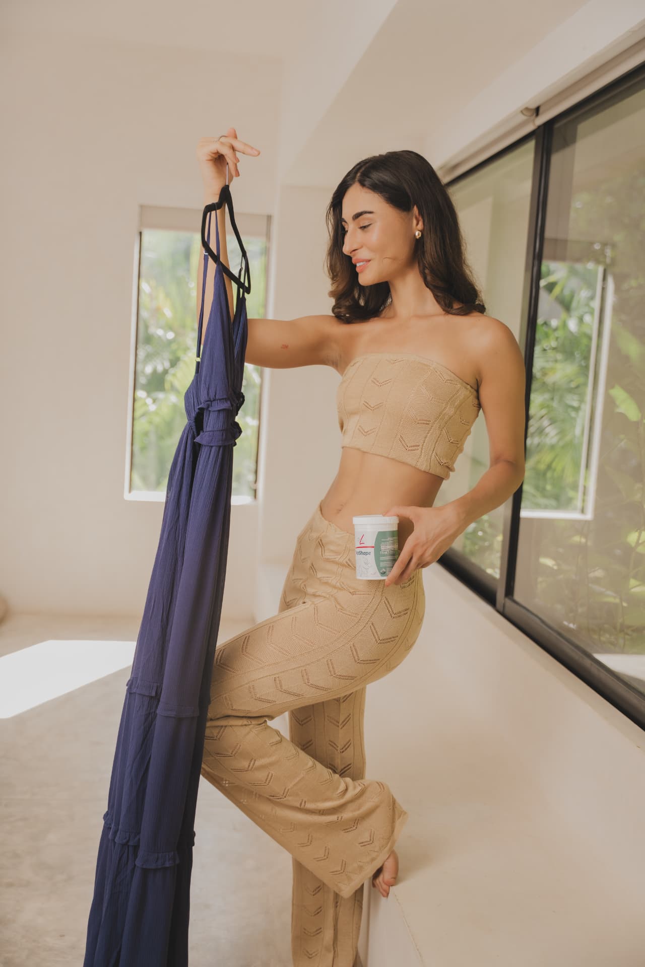 Vrouw kiest thuis een outfit met een pot FitLine TopShape in haar hand