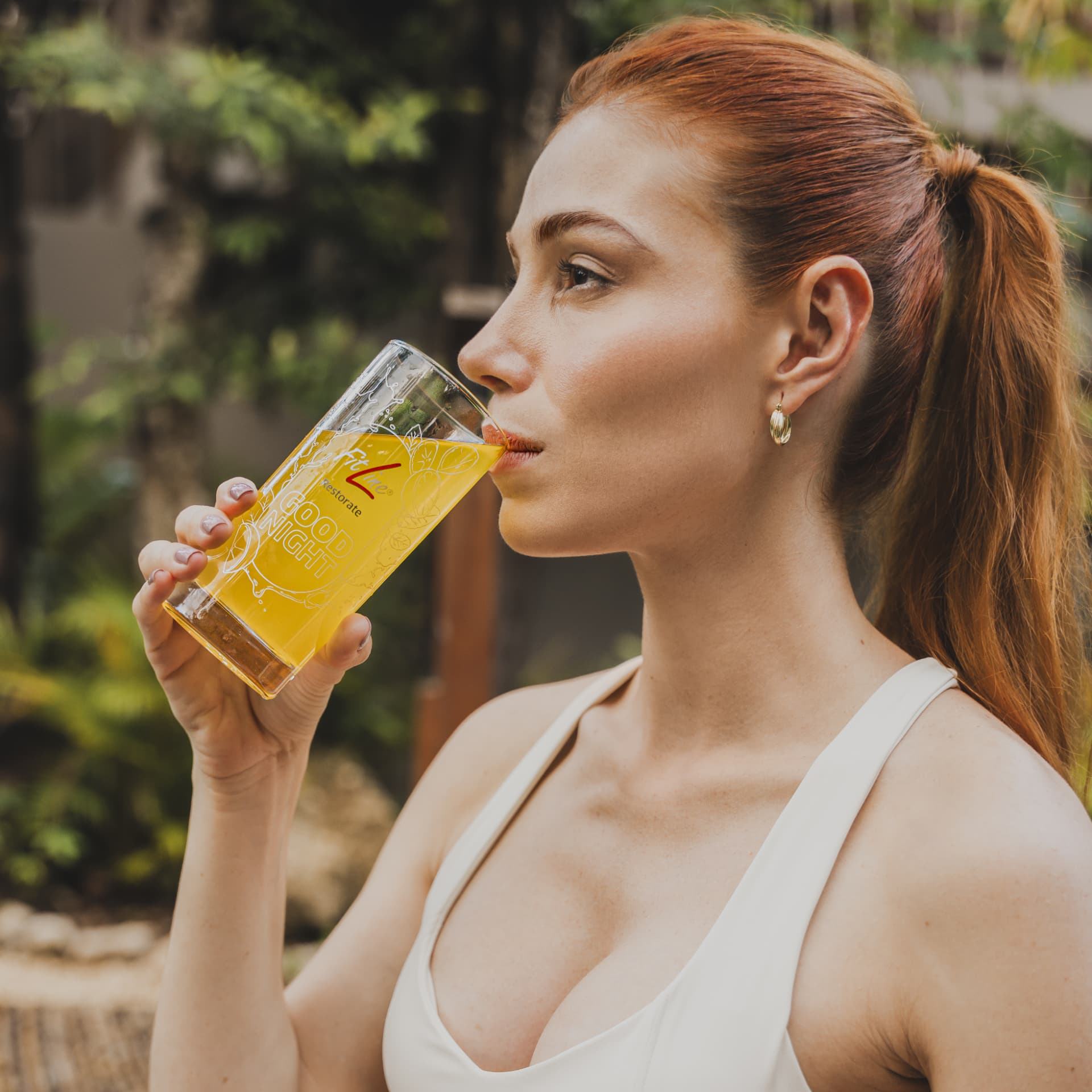 Vrouw die een glas FitLine Restorate Good Night Citrus drinkt in de tuin