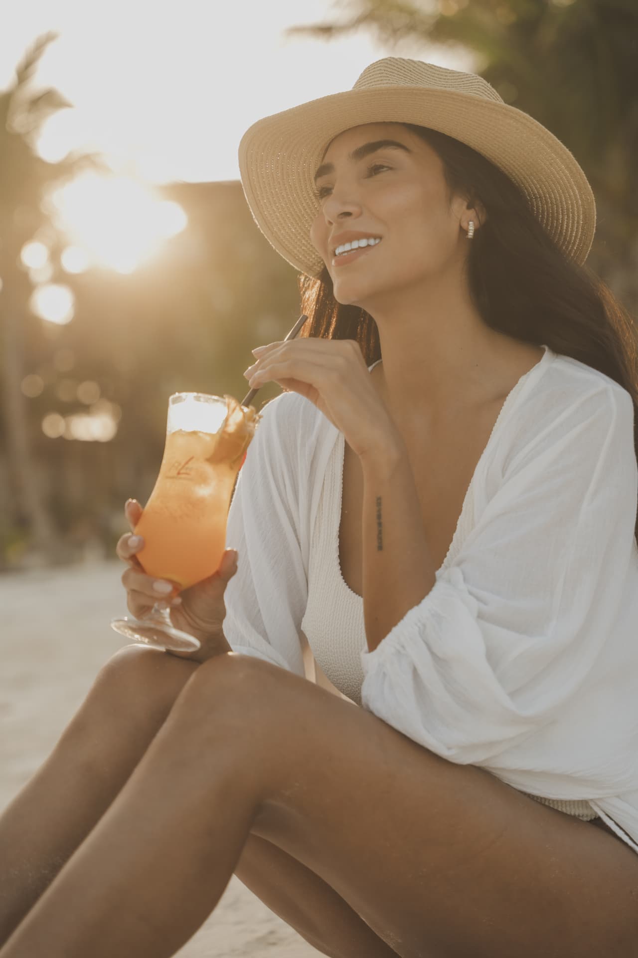 Vrouw zittend in het zand met een FitLine PowerCocktail in de hand
