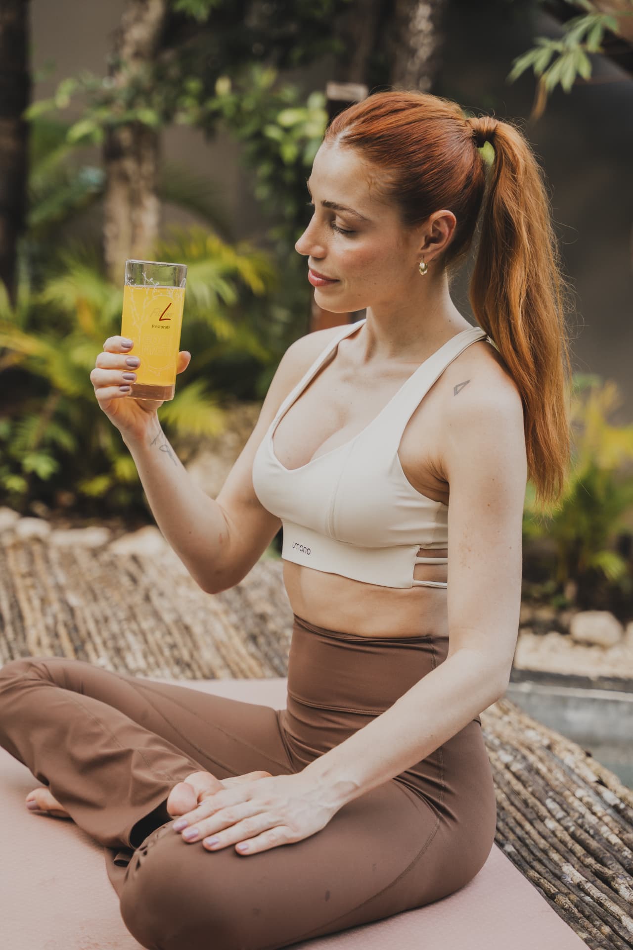 Vrouw zittend op een yogamat die een glas FitLine Restorate Citrus vasthoudt