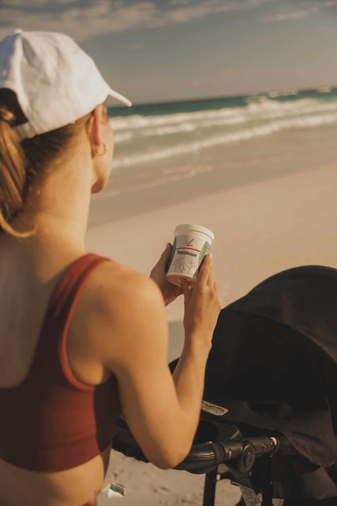 Vrouw met een pot FitLine TopShape in de hand met uitzicht op zee