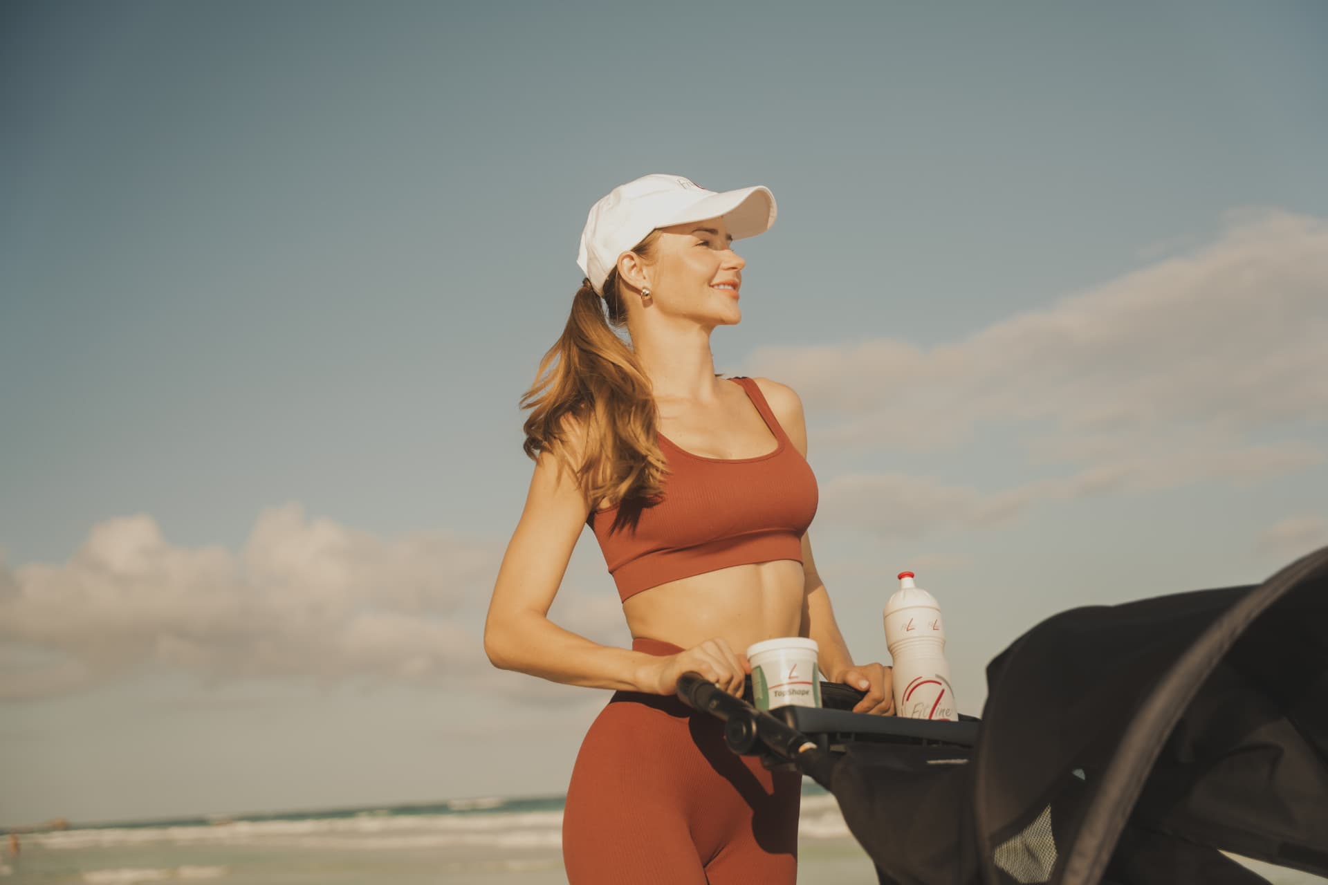 Vrouw in sportkleding buiten met FitLine TopShape en drinkbus op de kinderwagen