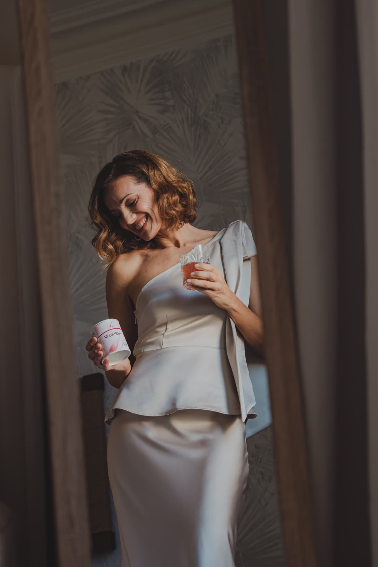 Vrouw in avondlook met een pot FitLine WOMEN+ en een glas in de hand