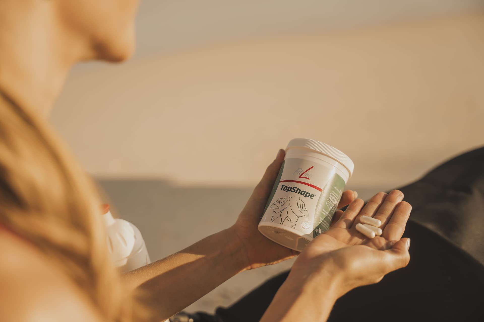 FitLine TopShape capsules in een handpalm naast de verpakking