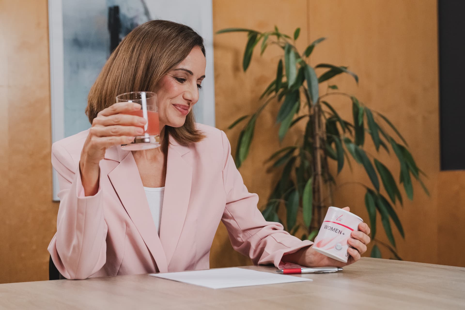 Vrouw met FitLine WOMEN+ en een glas op kantoor